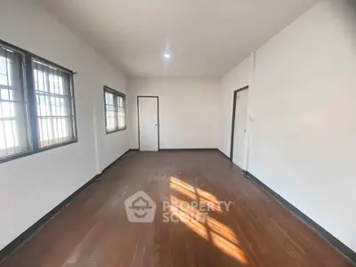 Spacious empty room with wooden flooring and large windows, ideal for customization.