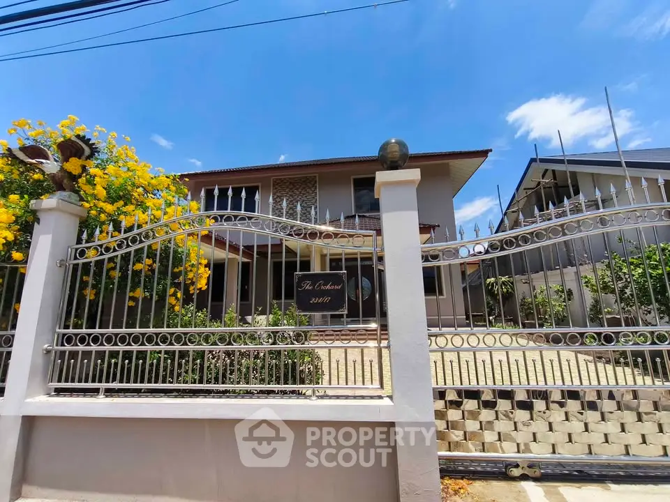 Charming two-story house with gated entrance and vibrant garden in sunny neighborhood.