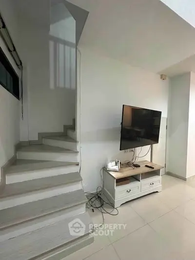 Modern living room with sleek staircase and mounted TV, perfect for contemporary living.