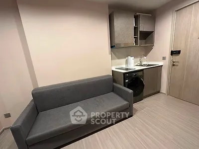Modern compact living space with sofa and kitchenette featuring washing machine and storage cabinets.