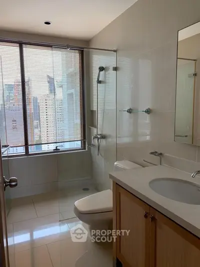 Modern bathroom with city view, glass shower, and sleek fixtures in a high-rise apartment.