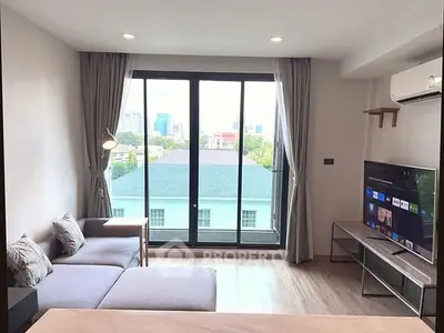 Modern living room with large windows and city view, featuring stylish furniture and a flat-screen TV.