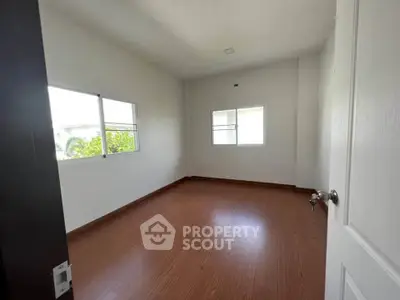 Spacious empty room with wooden flooring and large windows for natural light.