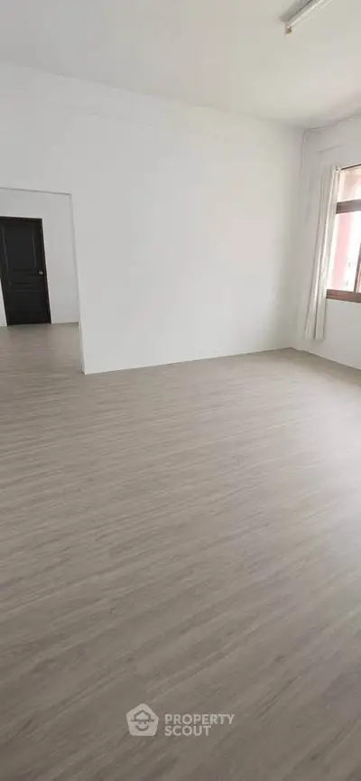 Spacious empty room with wooden flooring and large window, perfect for customization.