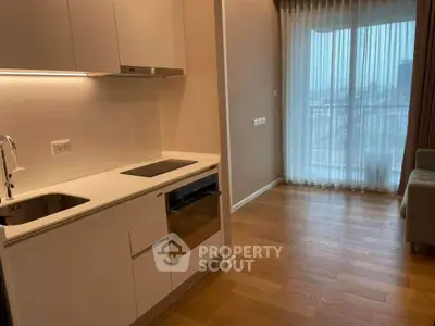 Modern kitchen with sleek cabinetry and open layout in a bright apartment with wooden flooring.