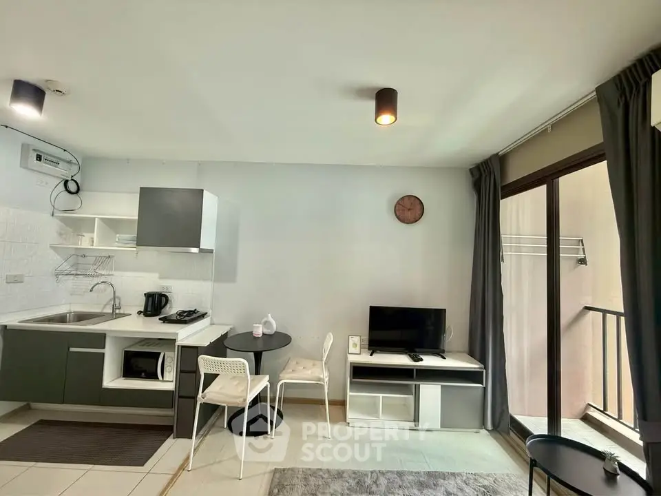 Modern open-plan living room with kitchen and balcony access, featuring sleek furniture and natural light.