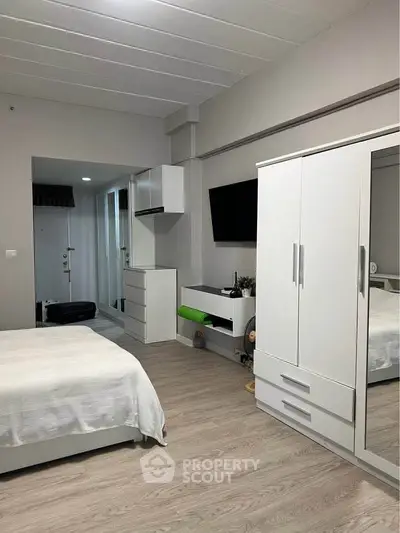 Modern bedroom with sleek white furniture and wall-mounted TV in a stylish apartment.