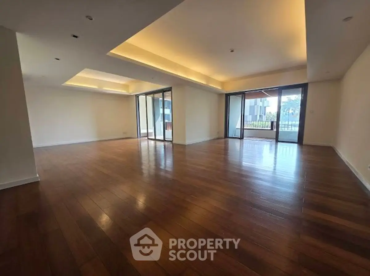 Spacious living room with wooden flooring and large windows offering natural light.