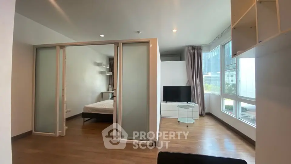 Modern studio apartment with sliding glass doors and large windows offering city views.