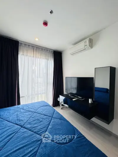 Modern bedroom with blue bedding, wall-mounted TV, and large window with curtains.