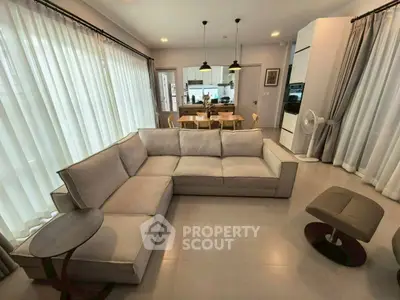 Spacious modern living room with elegant sofa and dining area, featuring large windows and stylish lighting.
