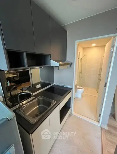 Modern compact kitchen with sleek cabinetry and adjacent bathroom in a stylish apartment.