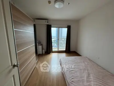 Spacious bedroom with wooden flooring and large window offering city views.