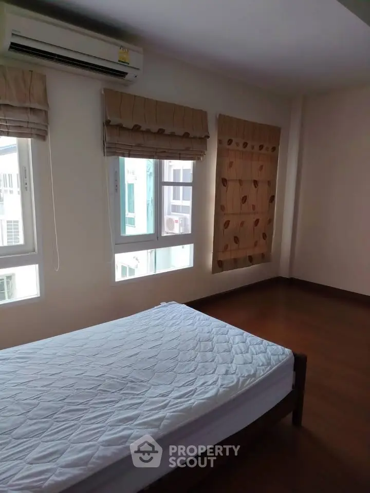 Spacious bedroom with wooden flooring and large windows for natural light.
