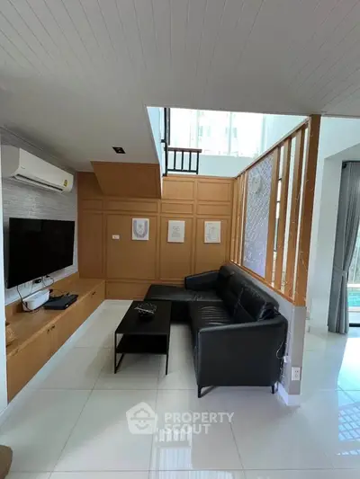 Modern living room with sleek black sofa, wall-mounted TV, and stylish wooden paneling.