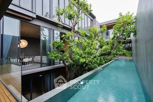 Modern luxury home with private pool and lush greenery, featuring floor-to-ceiling windows.