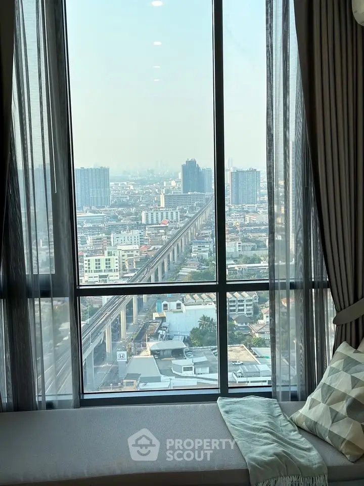 Stunning cityscape view from a high-rise apartment window with cozy seating area.