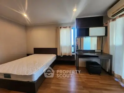 Spacious bedroom with wooden flooring and modern furniture in a well-lit apartment.