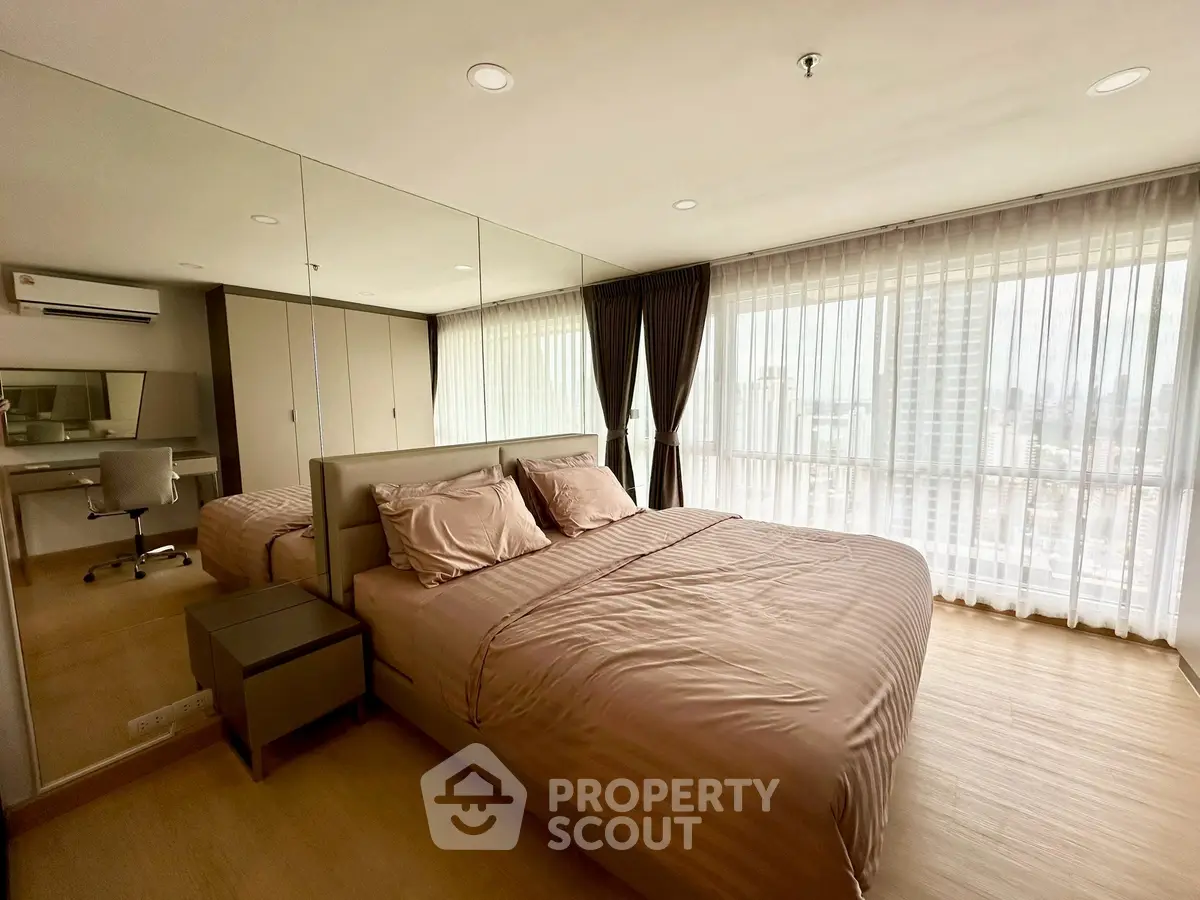 Spacious bedroom with city view and modern decor, featuring mirrored walls and large windows.