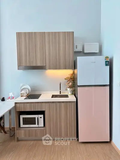 Modern compact kitchen with wooden cabinets, microwave, and fridge in a stylish apartment.