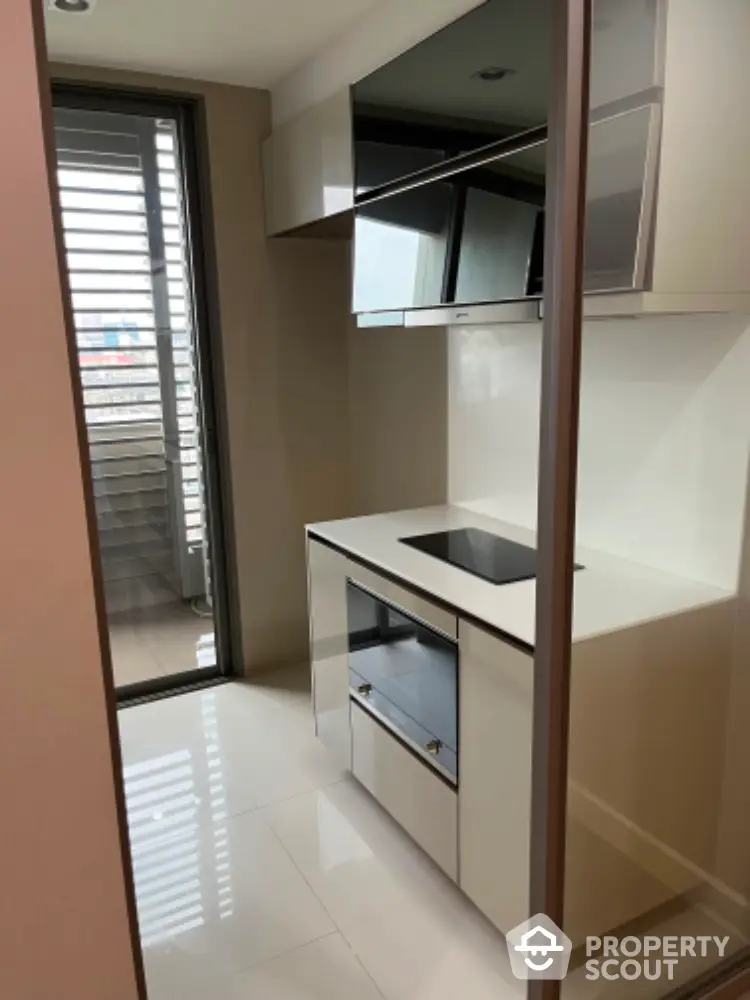 Modern compact kitchen with sleek cabinetry and induction cooktop, adjacent to a balcony with city views.