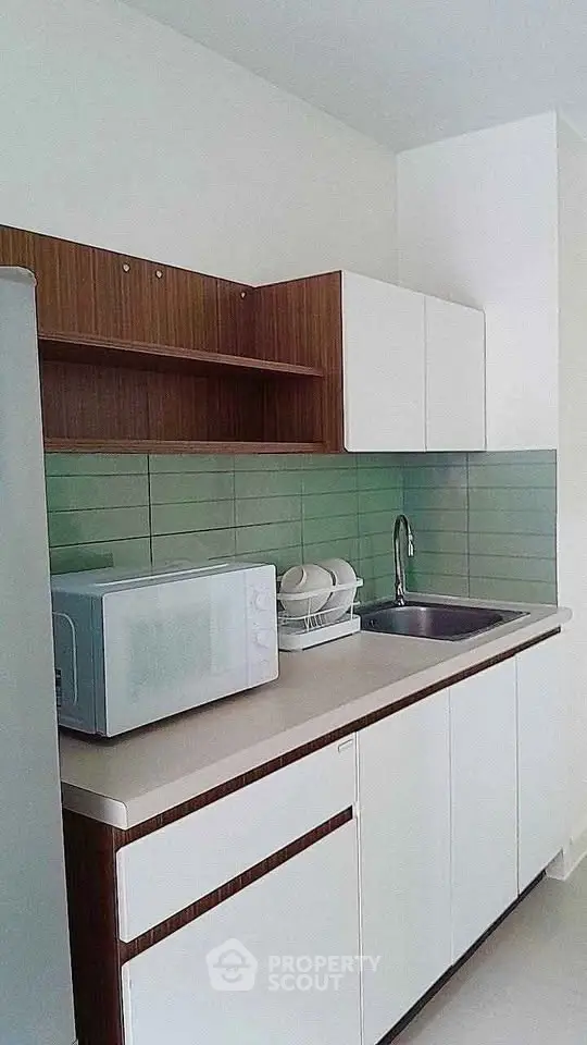 Modern kitchen with sleek cabinetry and green tile backsplash, featuring a microwave and sink.