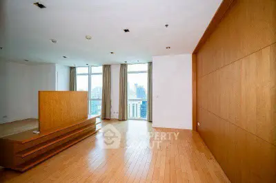 Spacious modern living room with wooden flooring and large windows offering city views.