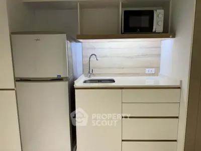 Modern compact kitchen with fridge, microwave, and sleek cabinetry