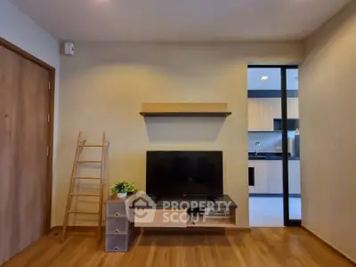 Modern living room with TV, wooden flooring, and open kitchen view.