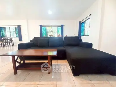 Spacious living room with modern black sofa and wooden coffee table, bright windows.