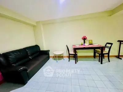 Cozy living room with black leather sofa and dining table, perfect for small gatherings.
