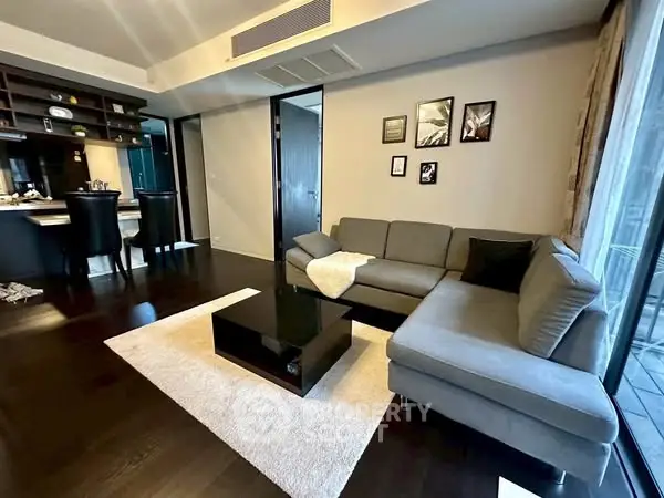 Modern living room with sleek furniture and open kitchen layout, featuring dark wood flooring and stylish decor.