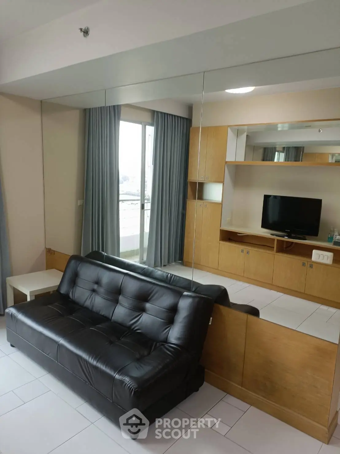 Modern living room with sleek black leather sofa and mirrored wall, featuring built-in wooden cabinets and natural light.