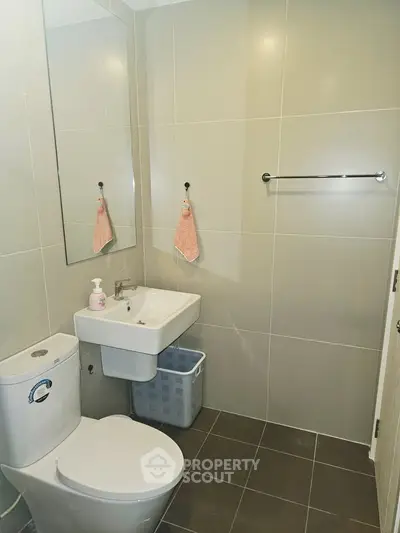 Modern bathroom with sleek fixtures and neutral tiles, featuring a compact sink and toilet.