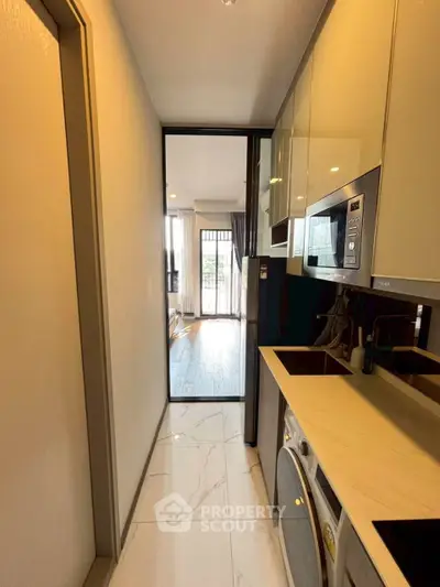 Modern compact kitchen with sleek appliances and open layout leading to a bright living area.