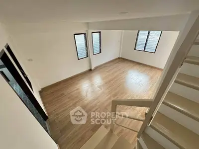 Spacious empty room with wooden flooring and staircase, ideal for customization.