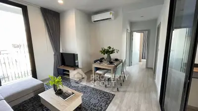 Modern living room with dining area, featuring sleek furniture and natural light from large windows.