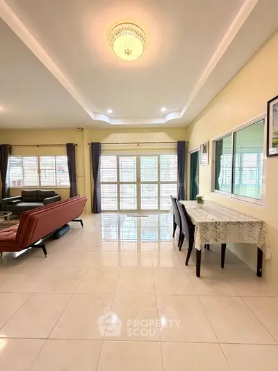 Spacious living room with elegant chandelier and large windows, featuring modern furniture and dining area.