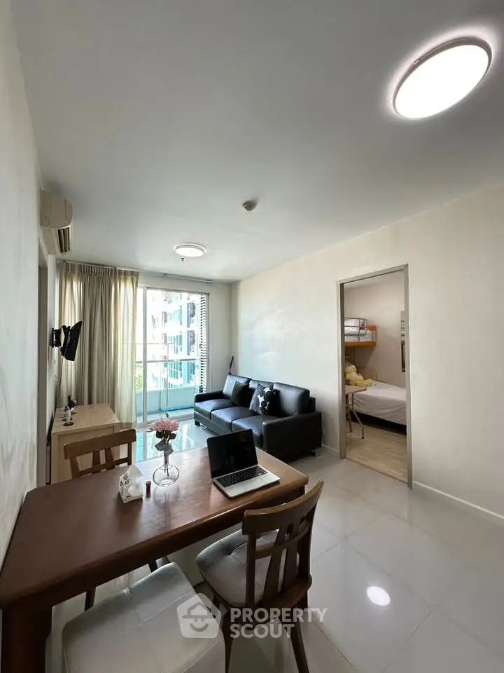 Modern living room with sleek furniture and natural light, featuring a cozy workspace and balcony view.