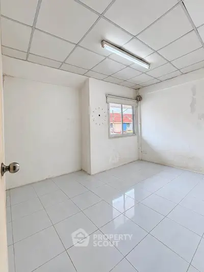 Spacious empty room with tiled floor and natural light from window.
