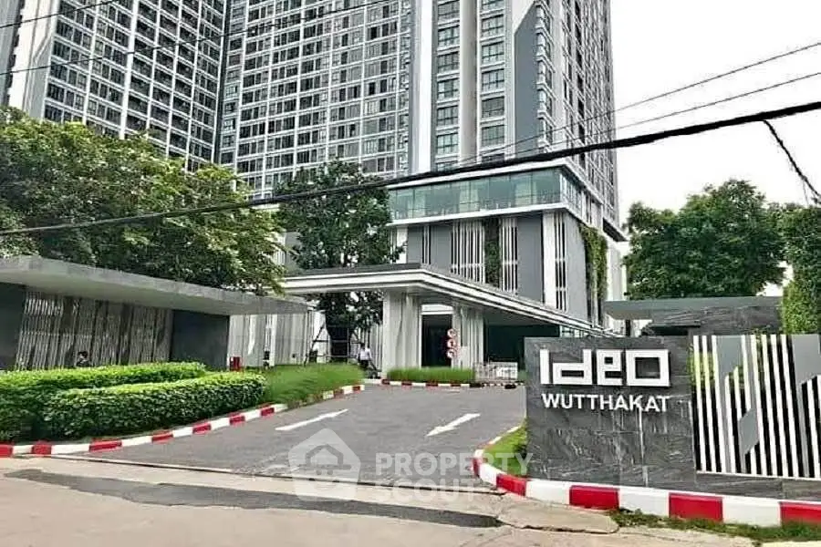 Modern high-rise building entrance with lush greenery and sleek design at Ideo Wutthakat.