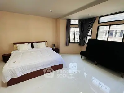 Spacious bedroom with large windows and modern furnishings in a high-rise apartment.