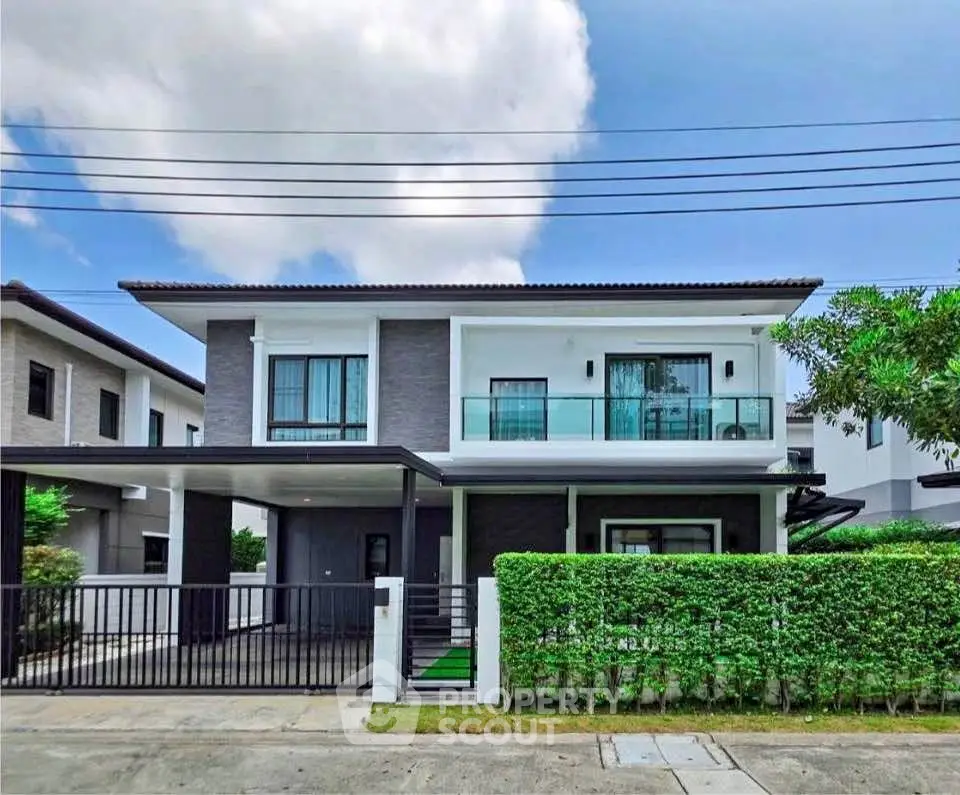 Modern two-story house with balcony and gated entrance in a suburban neighborhood.