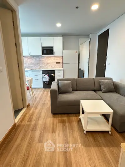 Modern open-plan living room with kitchen, featuring sleek furniture and wooden flooring.