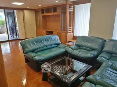 Spacious living room with green leather sofas and wooden cabinetry, featuring a glass coffee table and balcony access.