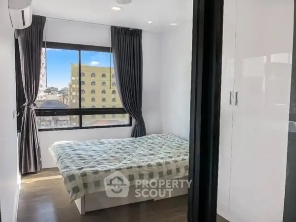 Modern bedroom with large window and city view, featuring sleek white wardrobe and cozy bed.