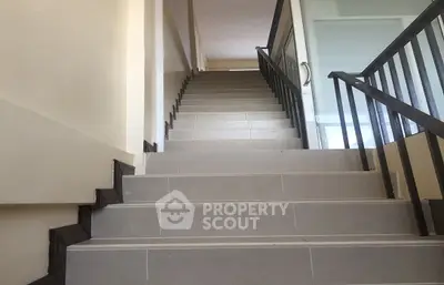 Pristine staircase in a modern residence with sleek metal railings and neutral-toned tiles, leading to a well-lit upper level.