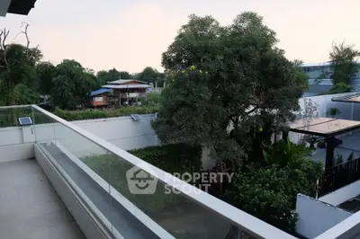 Spacious balcony with glass railing overlooking lush greenery and modern homes.