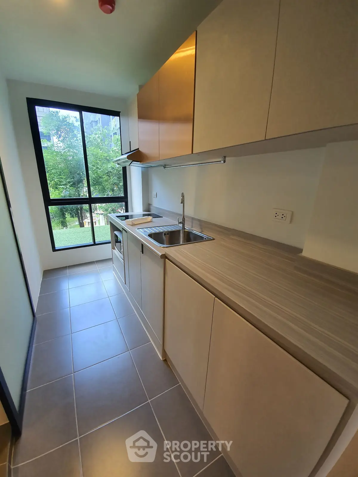 Modern kitchen with sleek cabinetry and large window offering garden view.