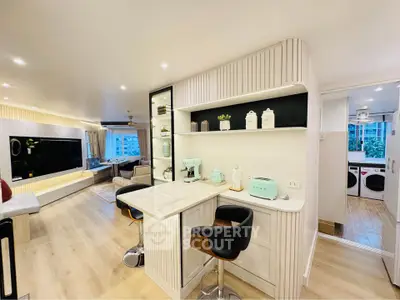 Modern open-plan living room with stylish kitchen and bar seating, featuring sleek appliances and elegant decor.